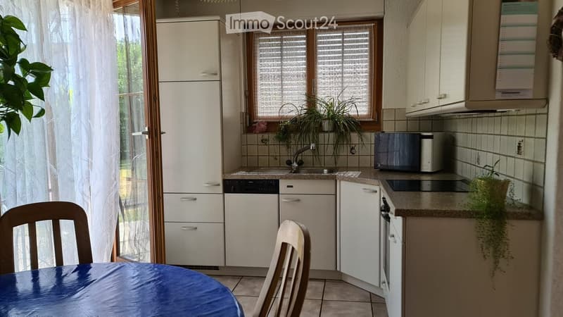 Modern kitchen with white cabinets, granite countertops, microwave, dishwasher, and a small dining area with a table and chairs.
