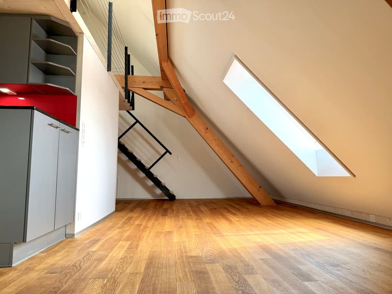 An attic space with wooden flooring, a modern staircase leading upwards, and a skylight window allowing natural light to enter.
