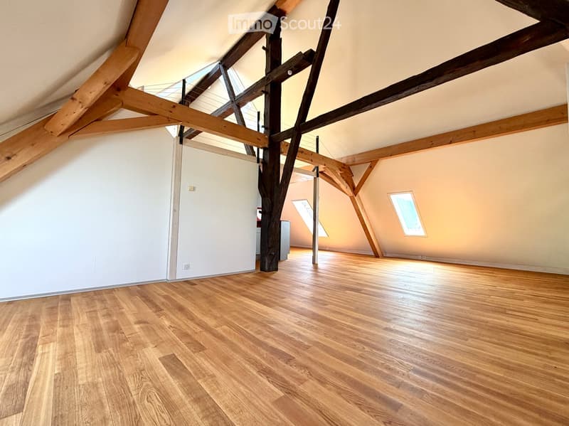 Empty attic space with wooden beams, wooden flooring, and skylight windows.