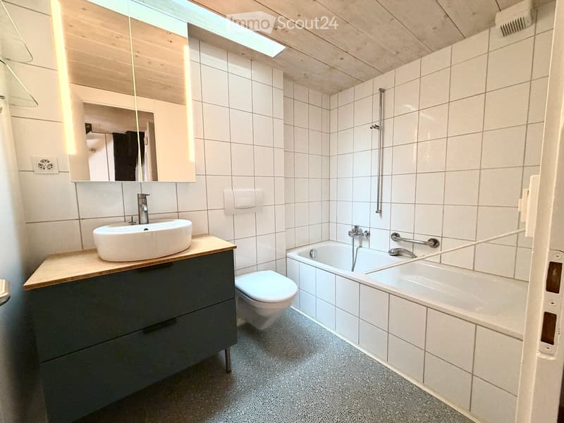 Modern bathroom with white tiled walls, a wooden countertop sink, a toilet, a bathtub, and a large mirror above the sink.