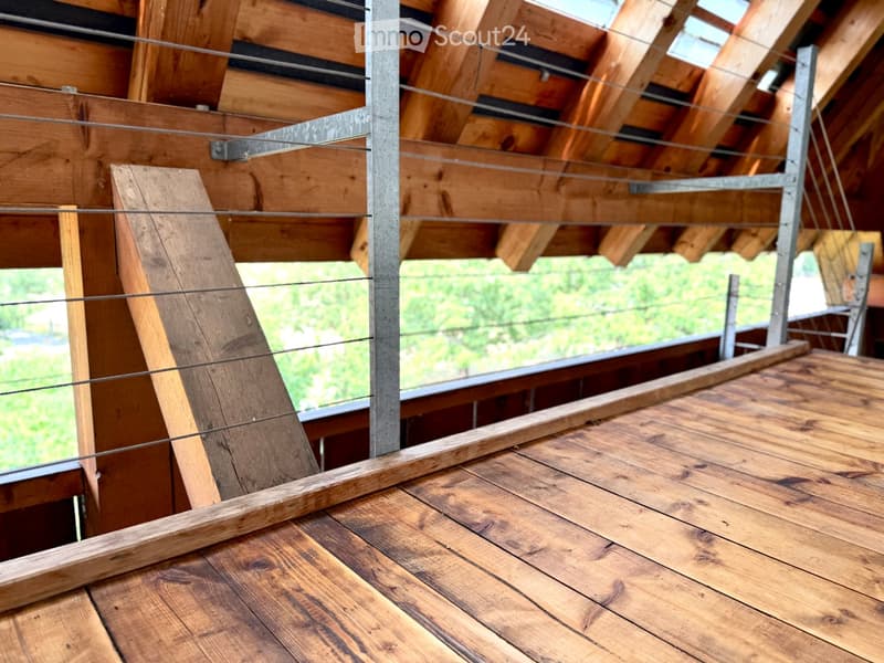 Wooden deck with metal railings and exposed wooden beams, offering a view of greenery outside.