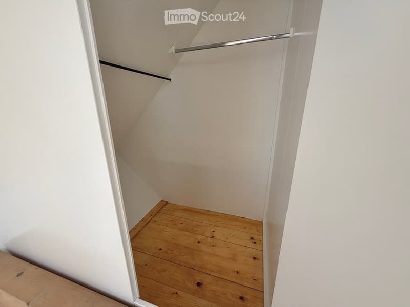 Empty room with wooden flooring and white walls, featuring a built-in closet with metal rods.