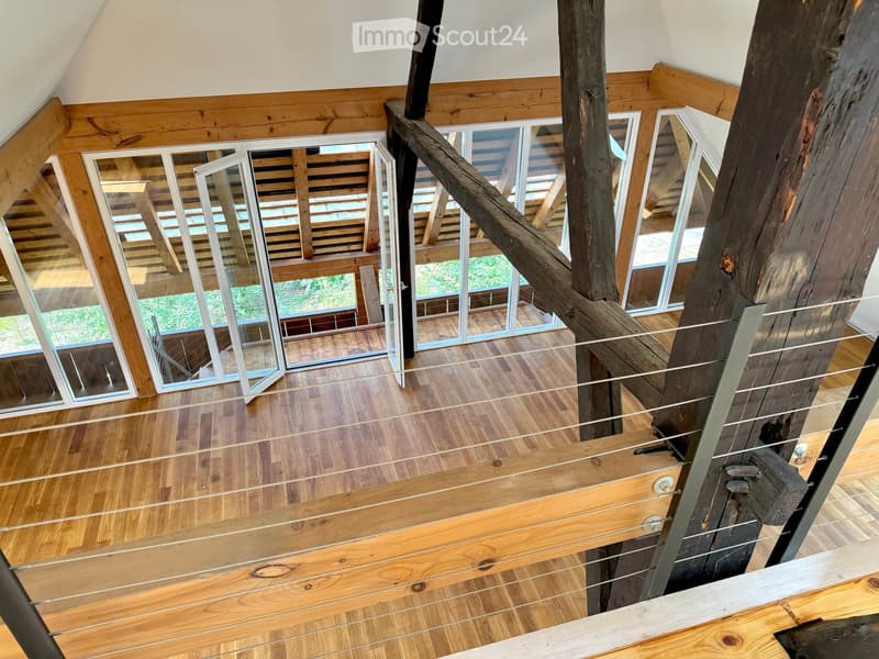 Open wooden staircase with glass railings and large windows, leading to a bright, airy space with wooden floors and exposed beams.
