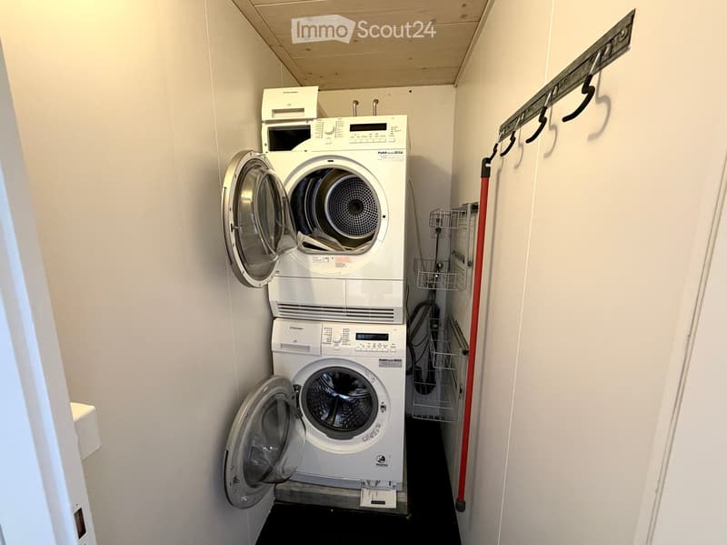Compact bathroom with a stacked washing machine and dryer unit, white walls, and a small shelf with cleaning supplies.