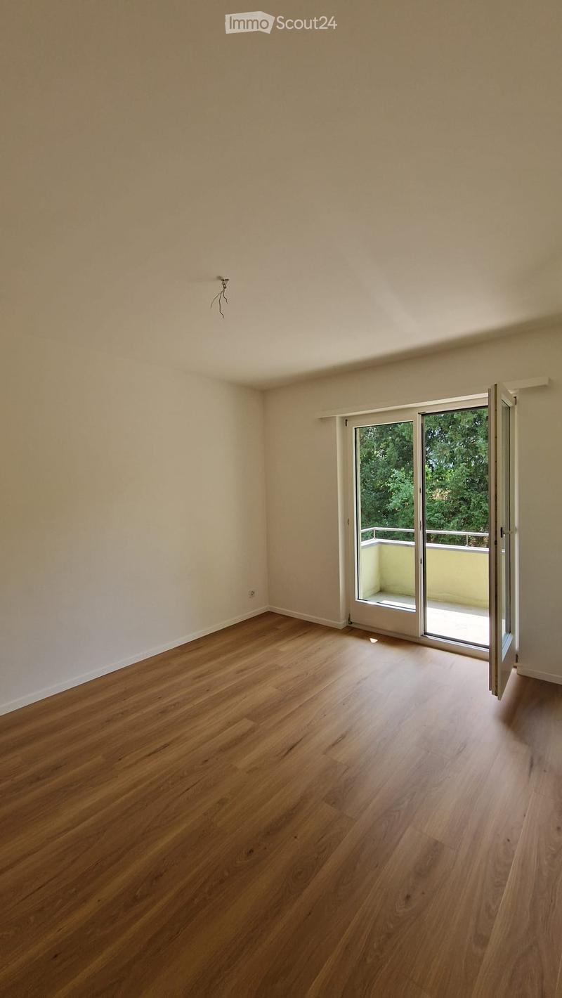 Empty room with light wooden flooring and white walls, featuring a sliding glass door leading to a balcony.