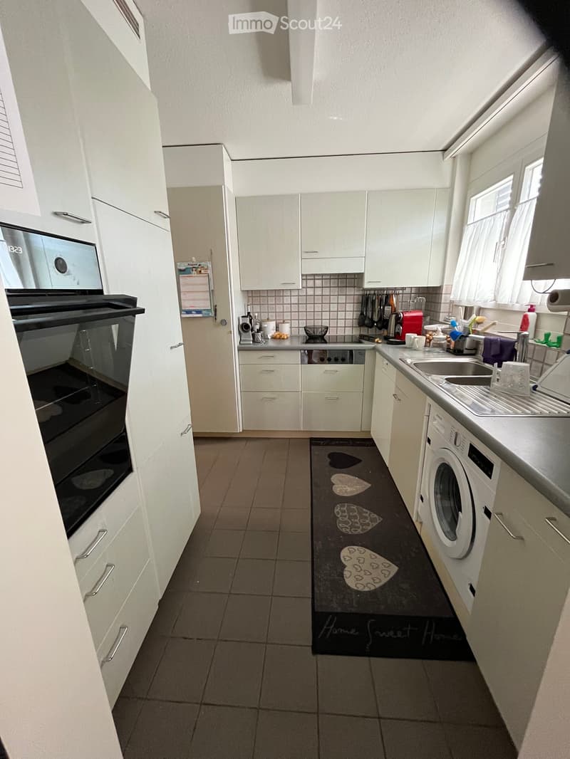 Modern kitchen with white cabinets, stainless steel appliances, and a black rug with heart designs.
