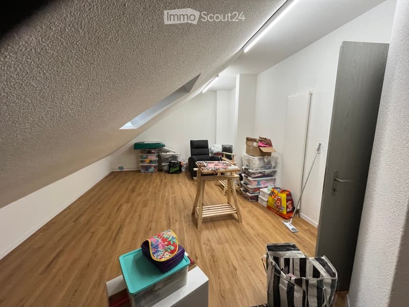Attic room with wooden flooring, slanted ceiling, and skylight. Contains a chair, small table, storage boxes, and bags.