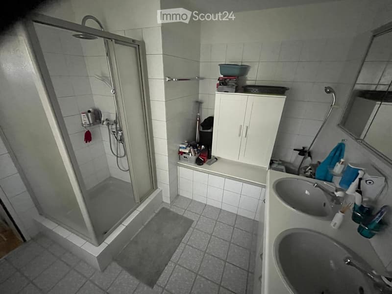 Bathroom with a glass-enclosed shower, sink, mirror, and cabinet. The space includes a towel and various toiletries.