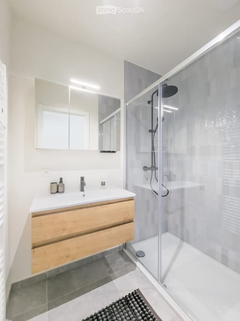 Modern bathroom with a wooden vanity, sink, mirror, and a glass-enclosed shower with a handheld showerhead.