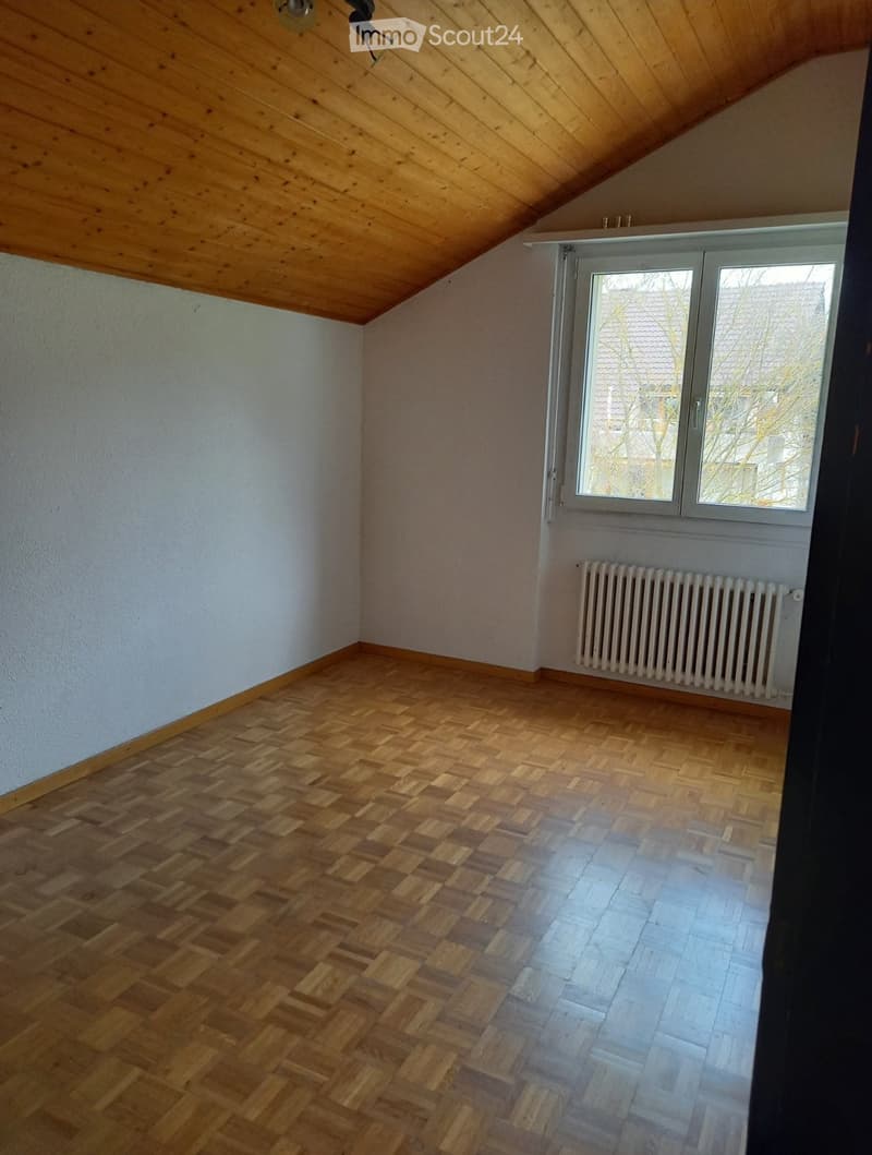 Empty room with wooden herringbone flooring, white walls, and a large window with a radiator below it.