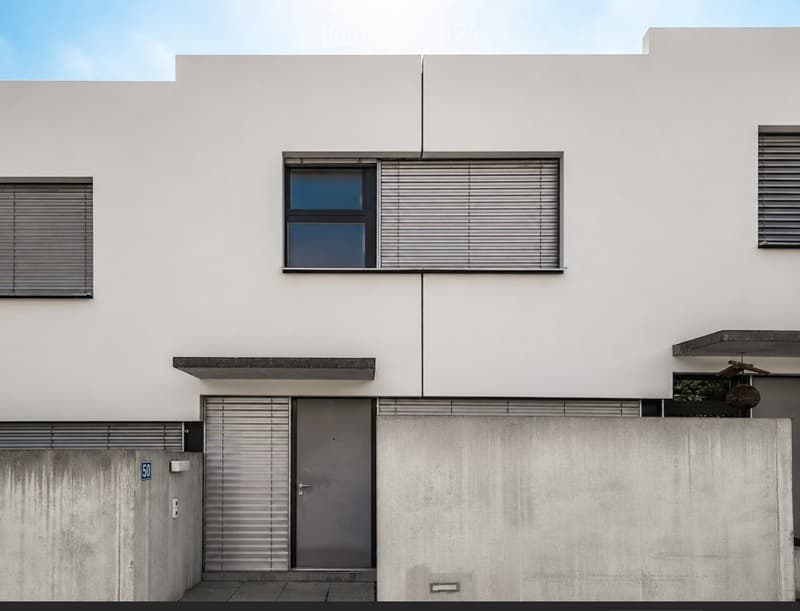Modern two-story white building with large windows, grey shutters, and a concrete base.