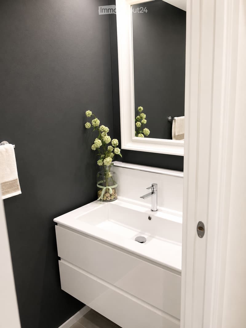 Modern bathroom with a white sink, chrome faucet, large mirror, and a vase with white flowers on the counter.