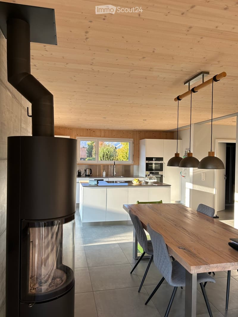 Modern kitchen and dining area with white cabinets, wooden dining table, pendant lights, and a wood stove.