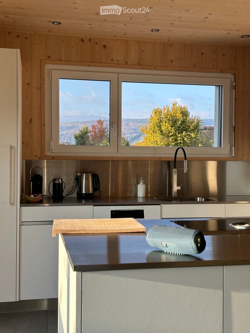 Modern kitchen with wooden cabinets, stainless steel appliances, and a large window overlooking a scenic landscape.