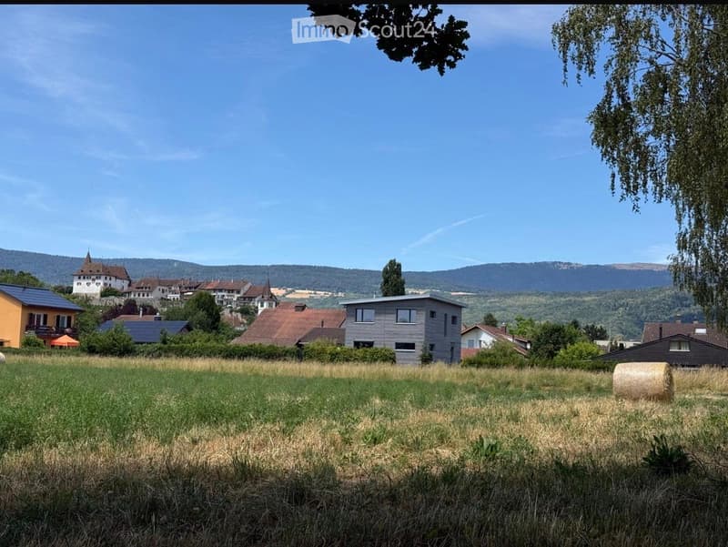 Rural landscape with scattered houses, green fields, and distant hills under a clear blue sky.