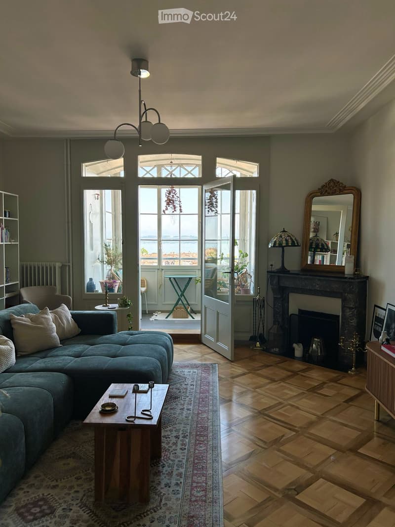 Living room with a blue sectional sofa, coffee table, fireplace, large windows with a view, and decorative items including a mirror and lamps.