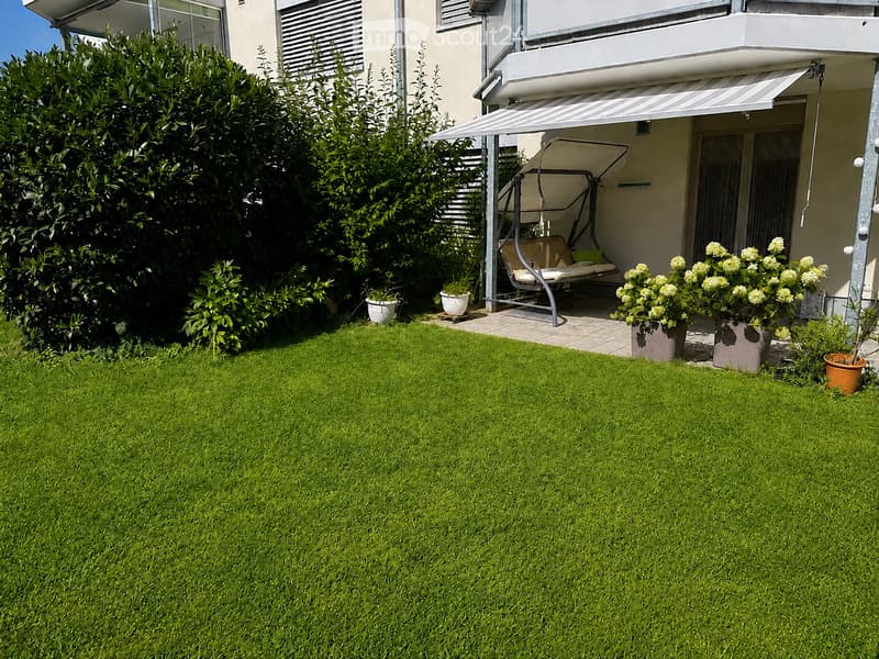 Well-maintained garden with green lawn, potted plants, and a hanging daybed near the house.
