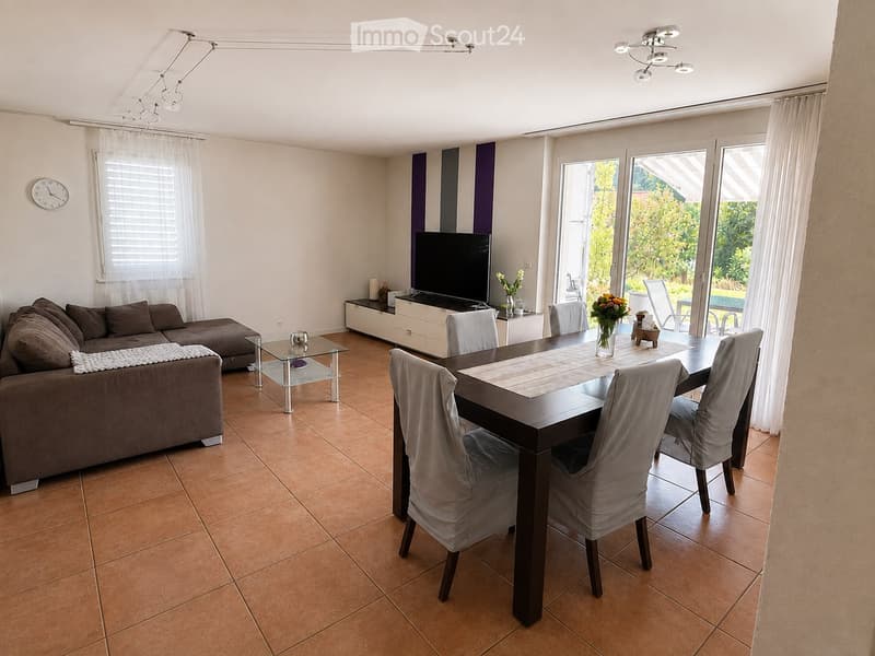 Modern living and dining area with a brown sectional sofa, glass coffee table, dark wooden dining table with four chairs, flat-screen TV on a white stand, and decorative vases on the table and TV stand.
