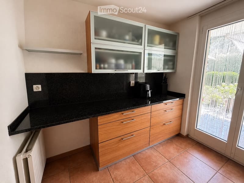 Modern kitchen with wooden cabinets, black granite countertop, and glass-front upper cabinets. Features a coffee maker and knife block on the counter.