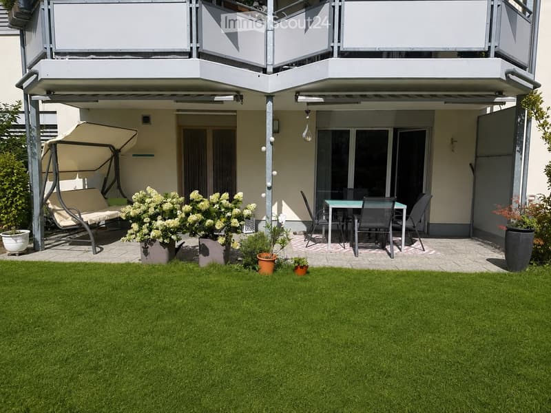 Garden with green lawn, swing chair, small table with chairs, and potted plants.