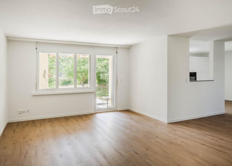 Empty room with light wooden flooring, white walls, large windows, and a sliding glass door leading to an outdoor area.