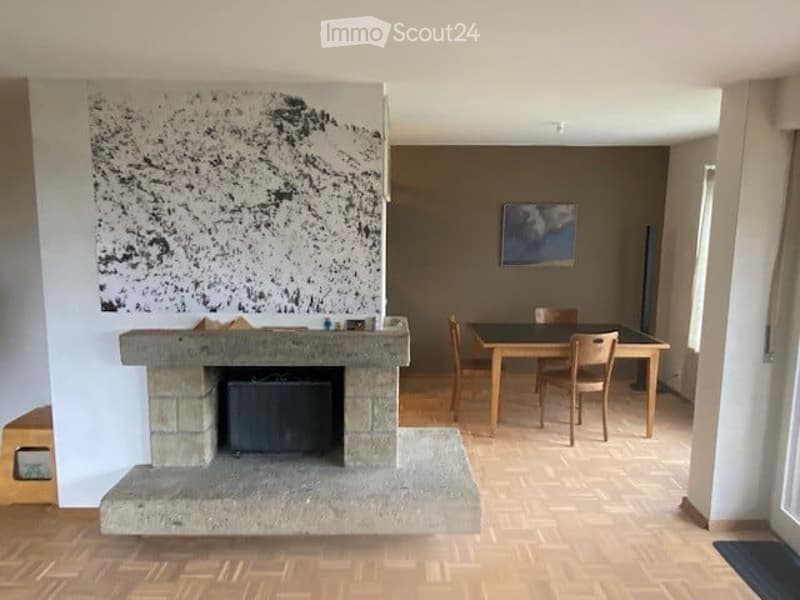 A modern living and dining area with a large fireplace, a dining table with chairs, and artwork on the walls.