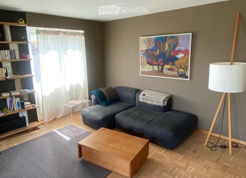 Modern living room with grey sectional sofa, wooden coffee table, bookshelf, floor lamp, and abstract painting on the wall.