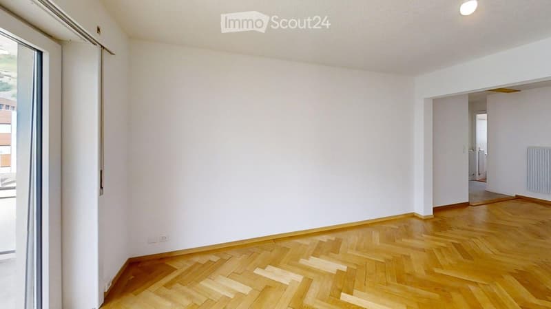 Empty room with light wooden flooring and white walls, featuring a large window and an open doorway leading to another room.