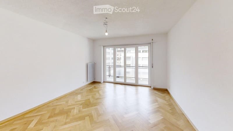 Empty room with wooden herringbone flooring, white walls, and large sliding glass doors leading to a balcony.