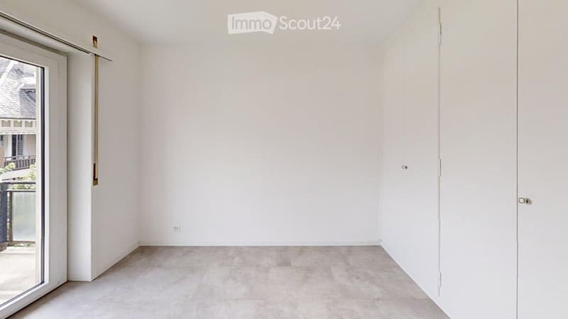 Empty room with white walls, light-colored tiled floor, and a large window with a view of the outside.