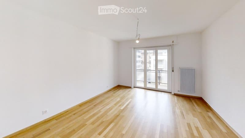 Empty room with wooden flooring, white walls, and a large sliding glass door leading to a balcony.