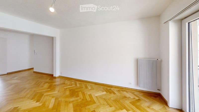Empty room with light wooden herringbone flooring, white walls, and a radiator on one wall. No furniture or personal items are present.