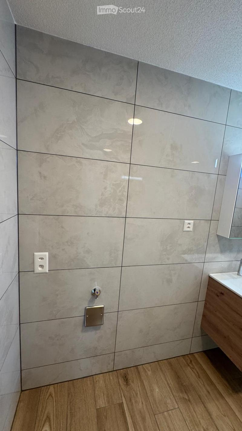Modern bathroom with marble-effect tiles, wooden flooring, and a sleek sink with a mirror.