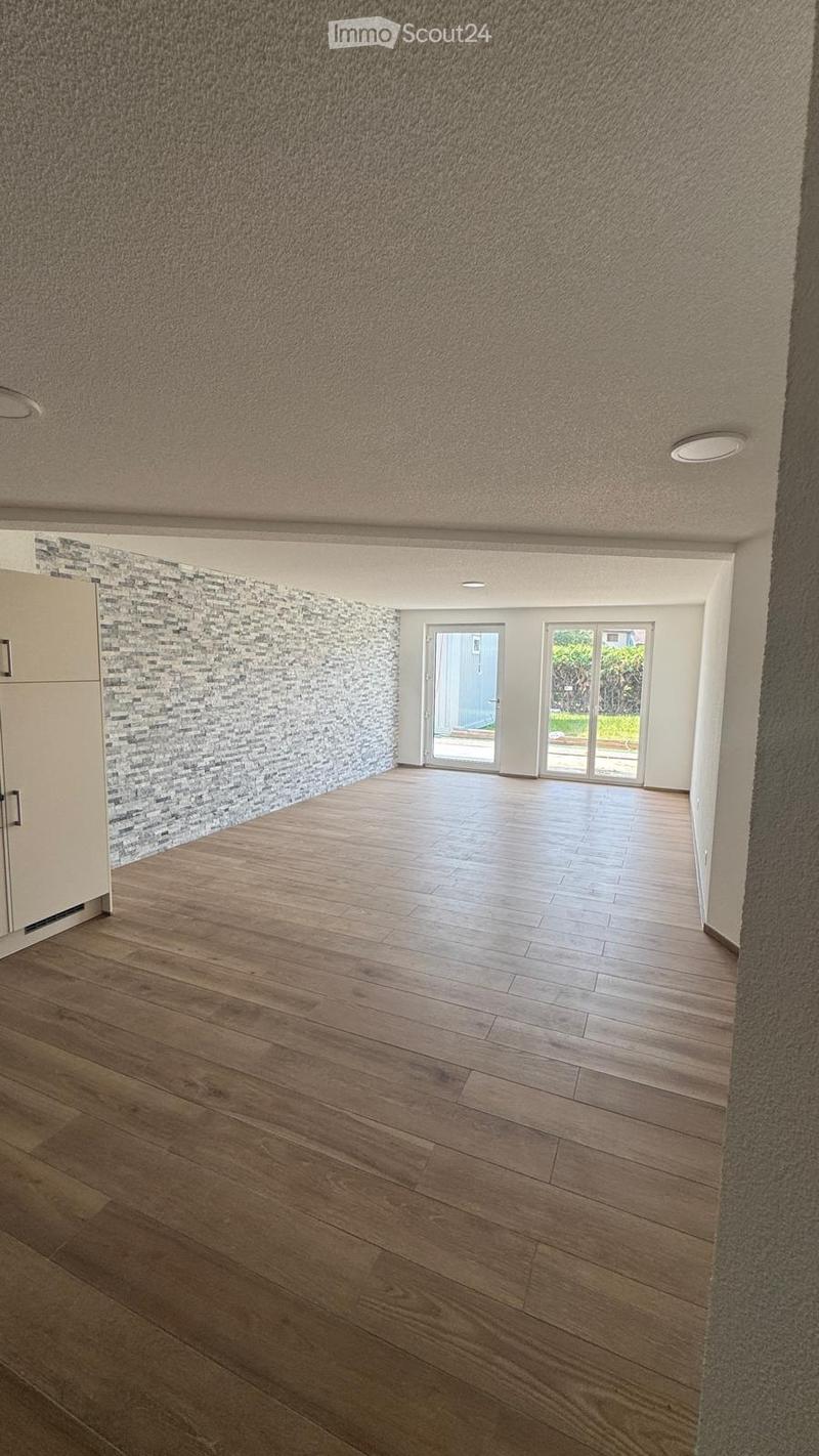 Empty room with wooden flooring, textured walls, and large glass doors leading to an outdoor area.