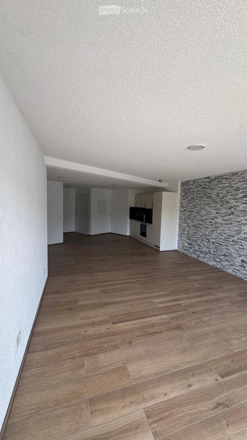 Open-plan living and dining area with wooden flooring, white kitchen cabinets, and a refrigerator visible in the background.