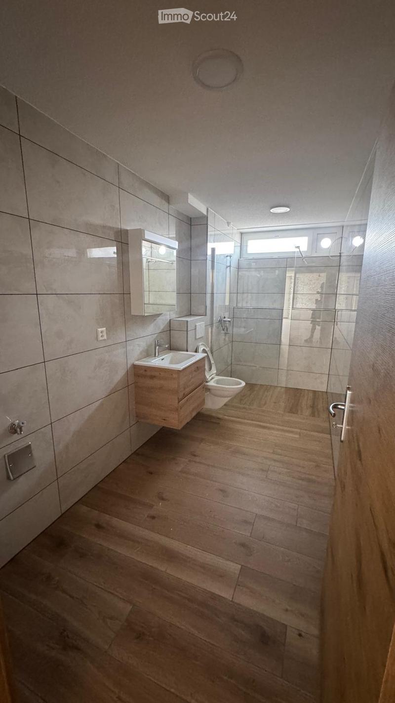 Modern bathroom with wooden flooring, a white sink, toilet, and a glass-enclosed shower area.