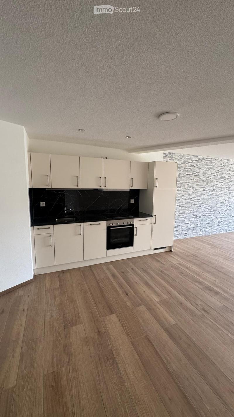 Modern kitchen with light-colored cabinets, a black countertop, and a wooden floor. The space includes a sink, an oven, and ample cabinet storage.