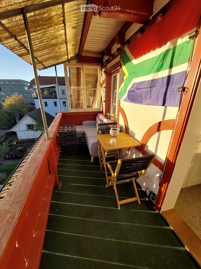 Balcony with green artificial turf, wooden table, two chairs, sofa, and a small decorative item.