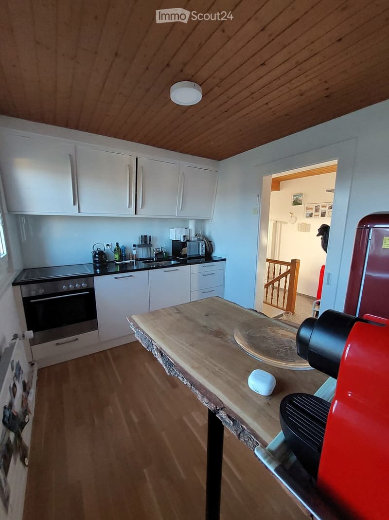 Modern kitchen with white cabinets, wooden countertops, and stainless steel appliances. Features an island with a coffee maker and a kettle on the counter.