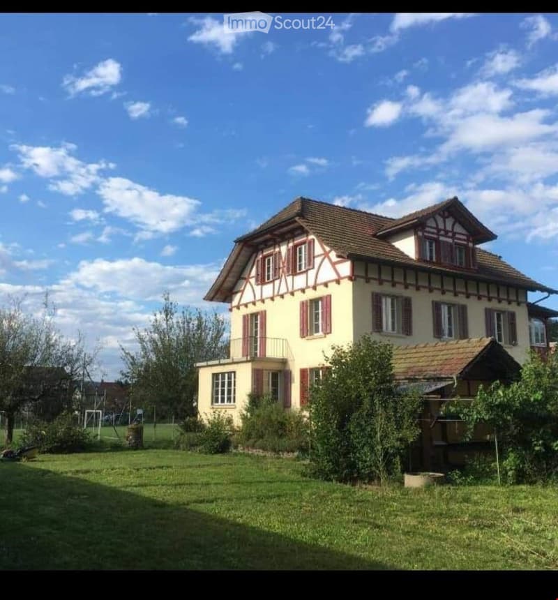 Two-story house with a half-timbered facade, multiple windows with shutters, and a well-maintained garden.