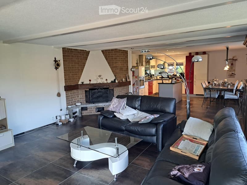Modern living room with a black leather sofa, glass coffee table, fireplace, and dining area with a table and chairs.