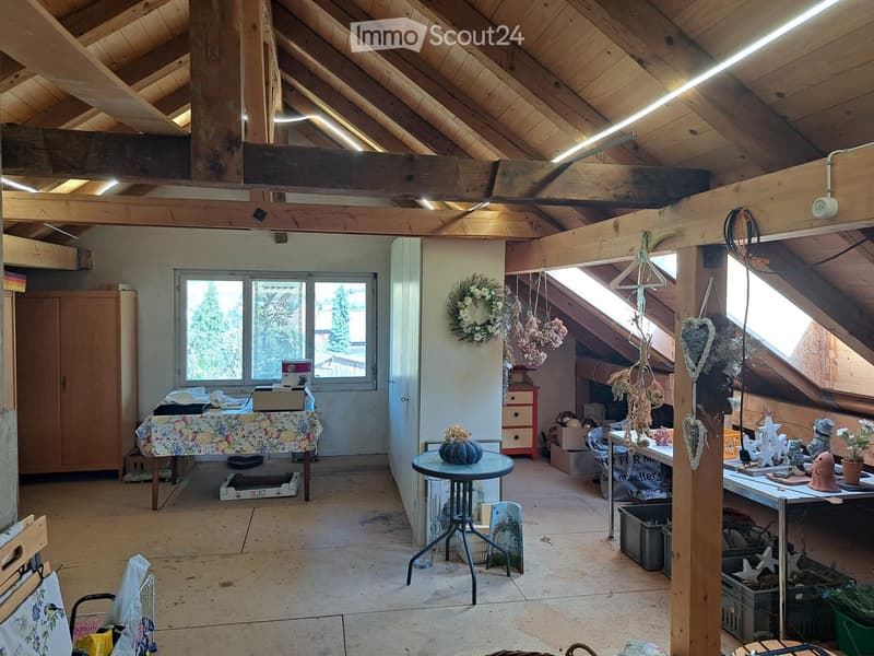 Loft-style room with wooden beams, exposed ceiling, large windows, and various furniture and decorative items.