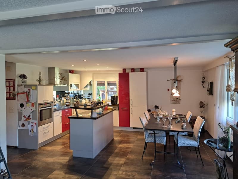 Modern kitchen with white and red cabinets, a central island, dining area with a table and chairs, and various kitchen appliances.