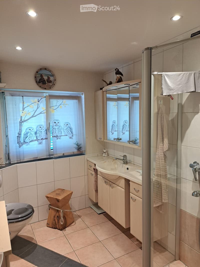 Modern bathroom with a sink, mirror, cabinet, wooden stool, toilet, and a glass shower enclosure with towels.