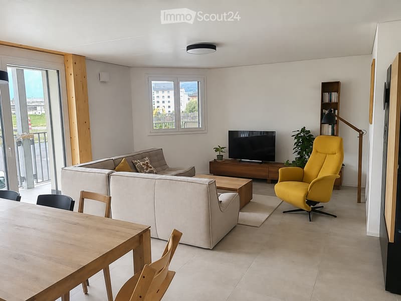 Modern living room with a grey sectional sofa, yellow armchair, wooden coffee table, dining table with chairs, TV, bookshelf, and plants.