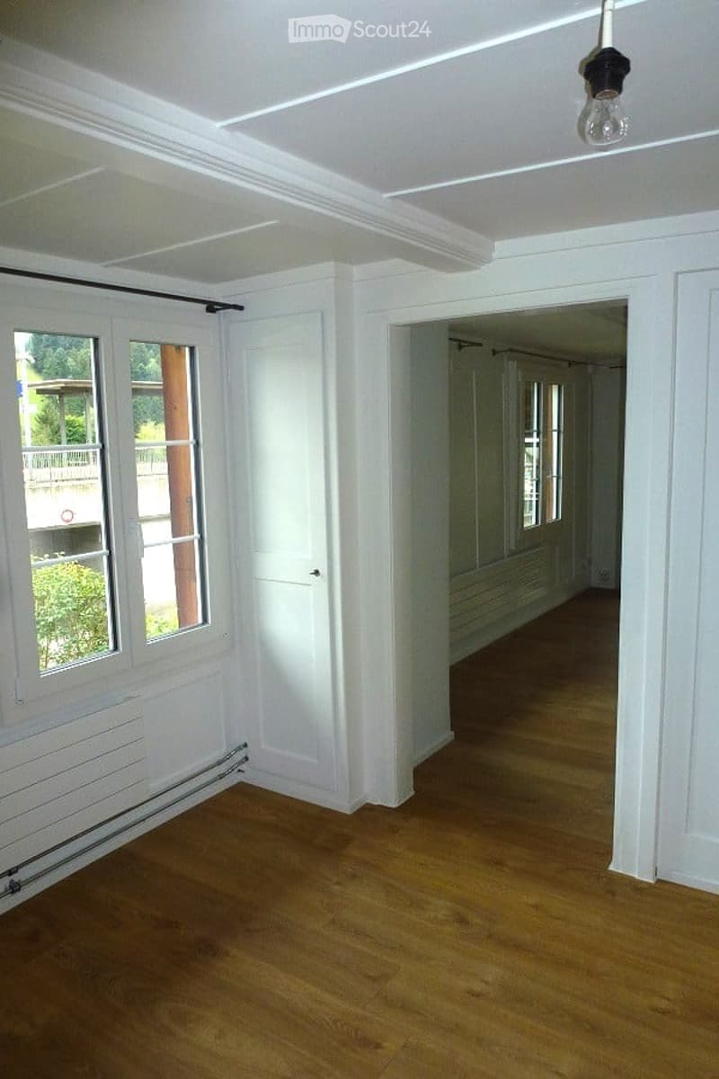 Empty room with wooden flooring, white walls, large windows, and a white cabinet. No furniture or equipment present.
