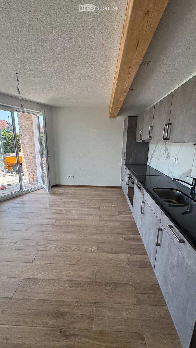 Empty kitchen with wooden flooring, grey cabinets, and a black countertop. Large sliding glass door leads to an outdoor area.