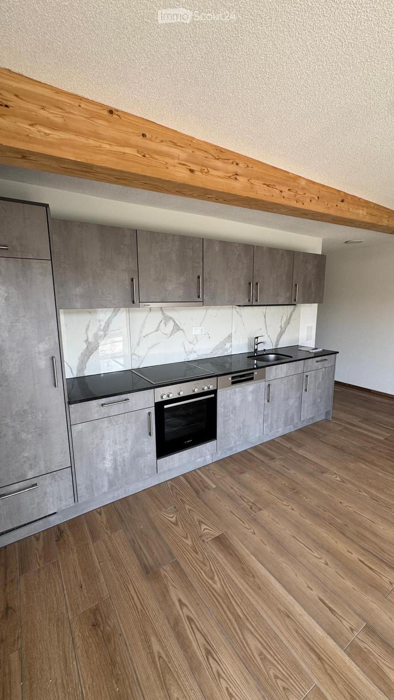 Modern kitchen with grey cabinets, wooden ceiling beam, marble backsplash, and wooden flooring.