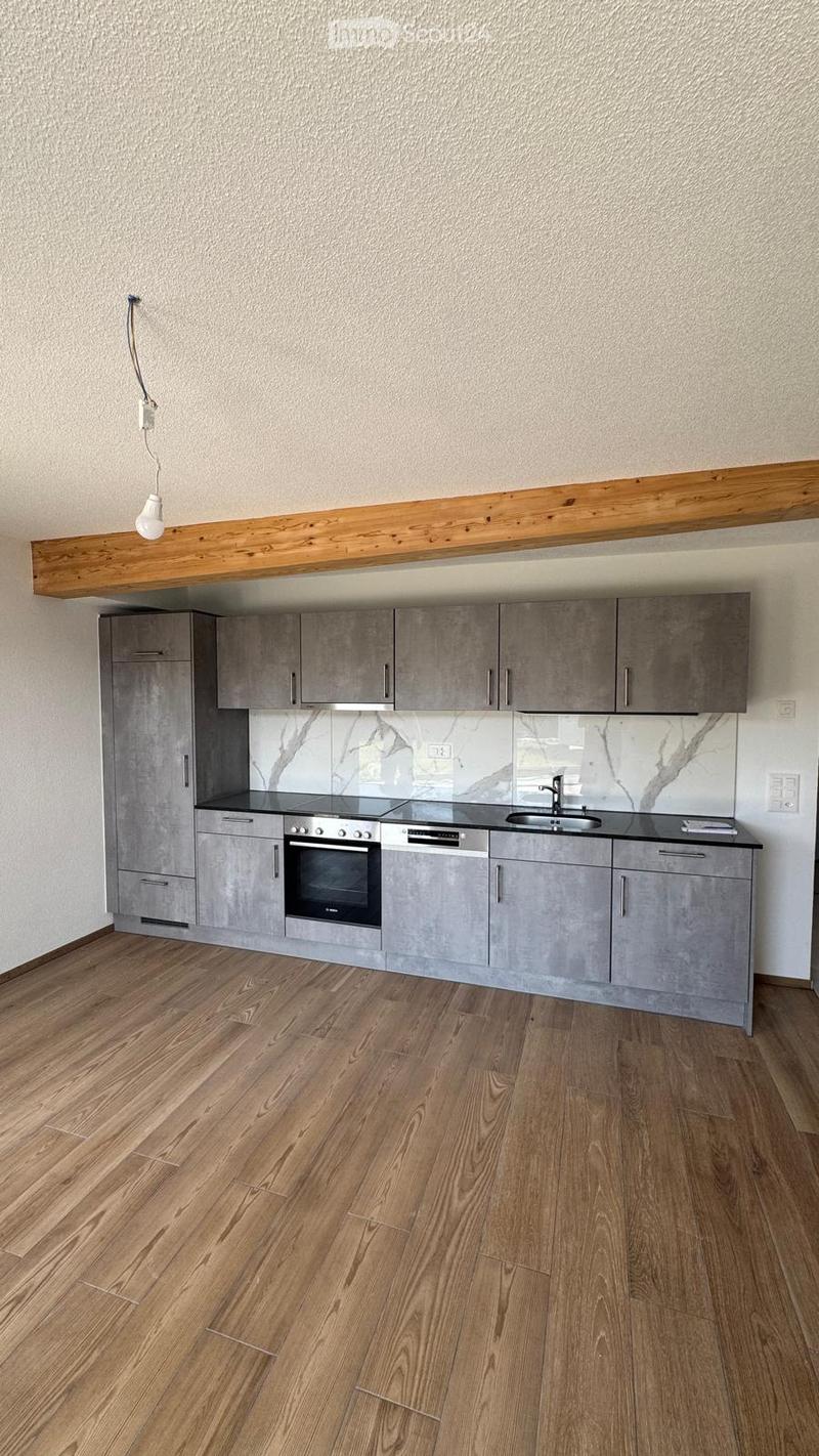 Modern kitchen with grey cabinets, wooden floor, and marble backsplash. Features an oven, sink, and faucet.