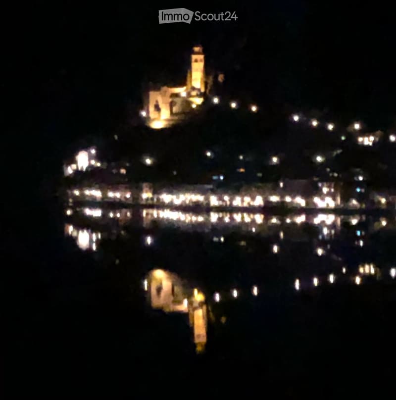 Nighttime view of a coastal town with illuminated buildings and lights reflecting on the water.